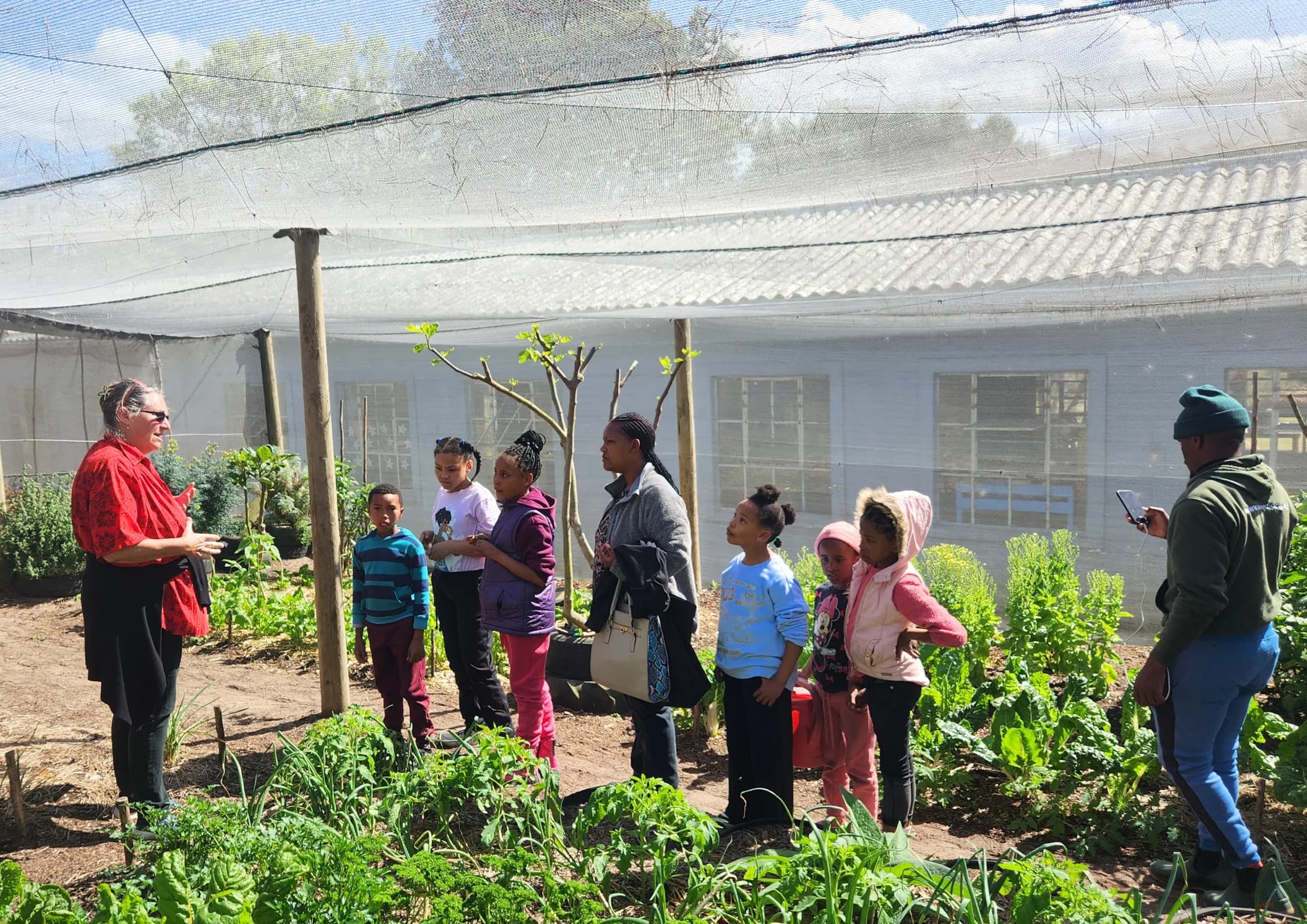 Children walk through a shaded pea and vegetable garden with netting overhead during a farm tour
